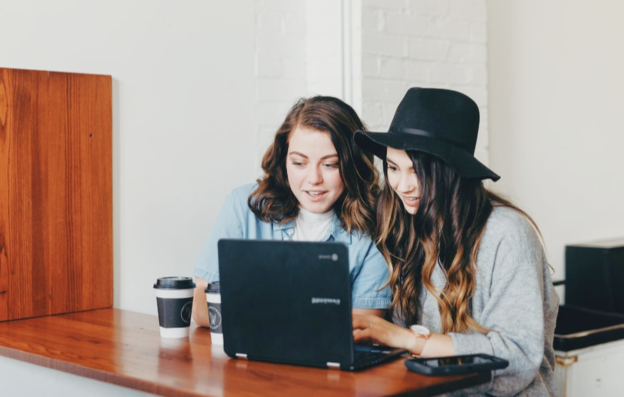 Two women working on a laptop and drinking coffee